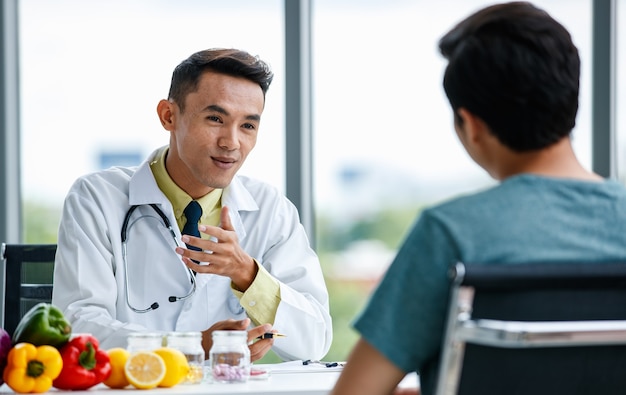 Il medico asiatico fornisce informazioni e consigli e spiega la prescrizione al paziente dell'uomo durante il lavoro in ospedale