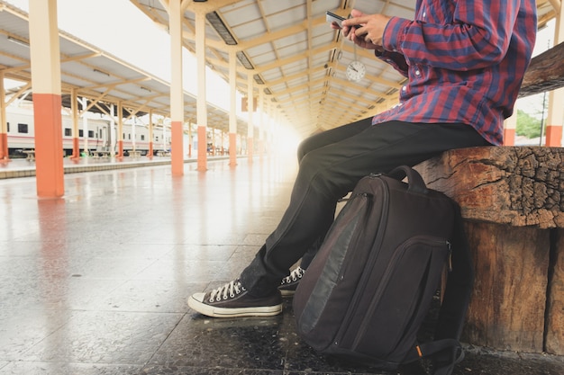 アジアの男性は電車を待っている間に携帯電話を使用しています