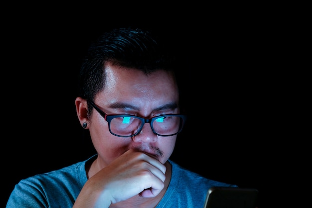 Foto gli uomini asiatici stanno usando il telefono o il tablet con una luce blu nelle tenebre, effetti concettuali della tecnologia.