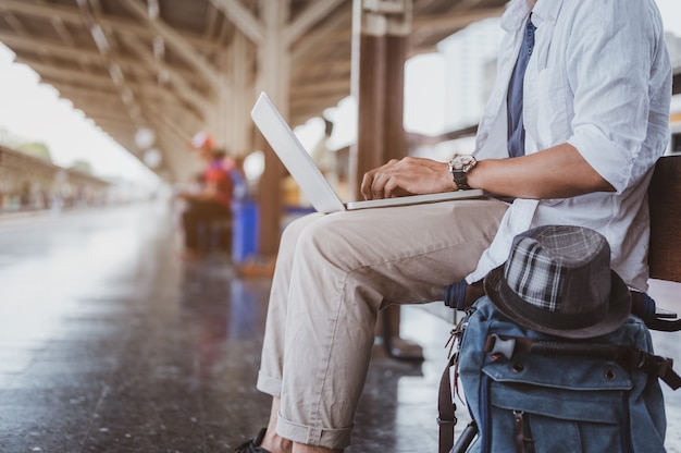 Asian men use their laptop to work while waiting to board the\
train to travel.holiday, journey, trip and summer travel\
concept.