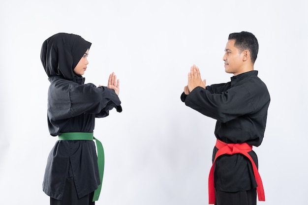 Asian men and women wearing pencak silat uniforms stand face to face with respect