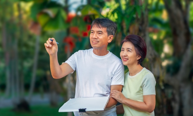 Asian middle-aged couple talking and designing garden plan together in backyard.