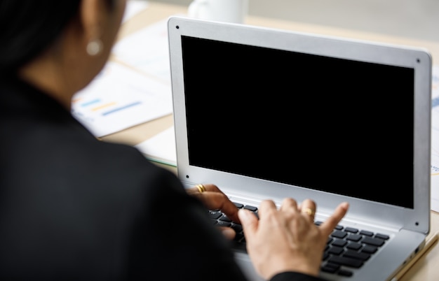 アジアの中年幸せな自信を持って女性の成功した女性秘書は、静かな会社のオフィスの部屋で一人でラップトップノートパソコンで情報を入力するワーキングデスクに座って正式なスーツを着ています。