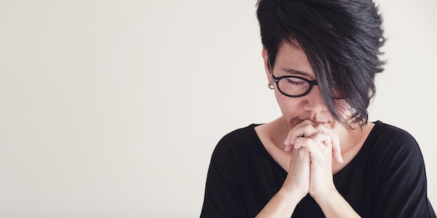 Donna di mezza età asiatica indossa occhiali pregando, concetto di speranza