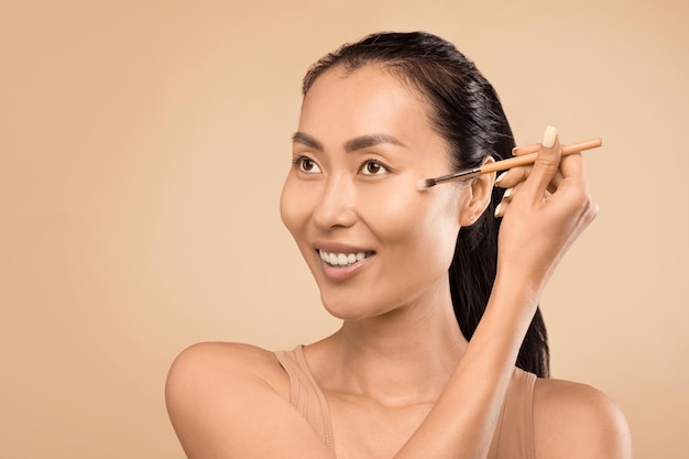 Asian middleaged woman beautifully applying nude makeup with highlighter brush