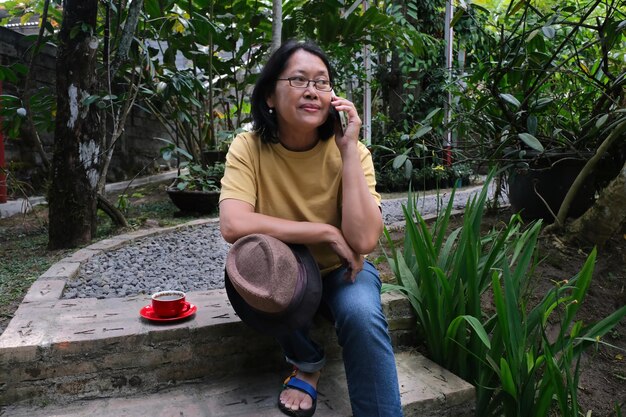 Asian middleaged woman sitting alone in the garden making a phone call with her smartphone