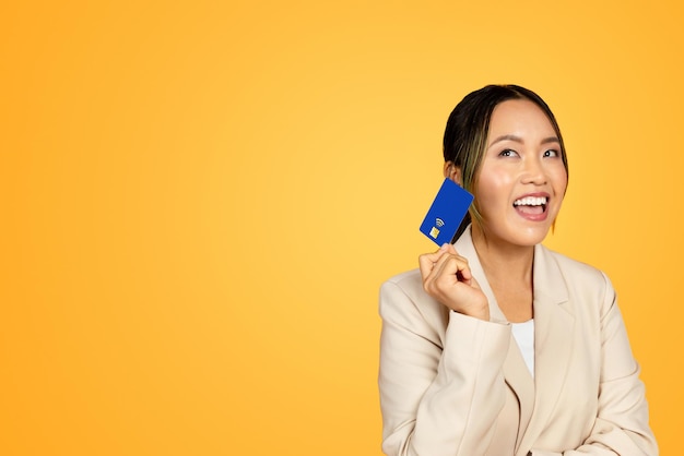 Asian millennial woman in suit confidently holding a credit card considering a purchase