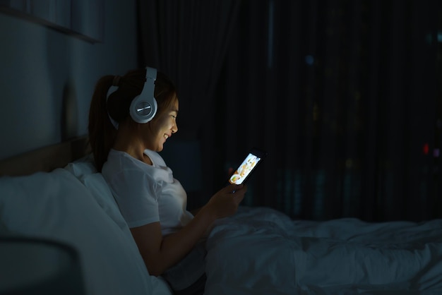 Photo asian mobile addict woman using digital tablet browsing the internet for watching movie or virtual meeting video call online with boyfriend on the bed before she sleeping at night