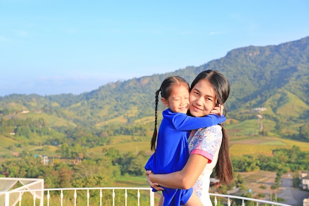 Asian mom cuddle her daughter with love on balcony at hillside.