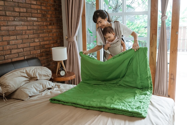 アジアのお母さんと赤ちゃんがベッドの上で毛布を掃除して配置します