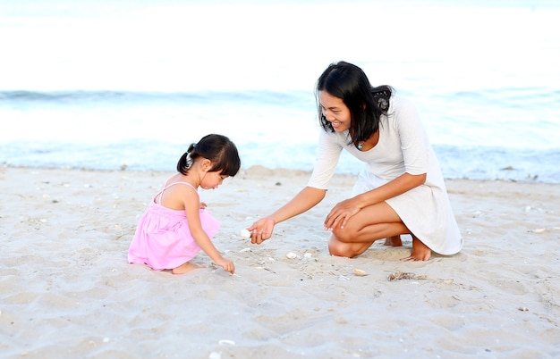 Asian mom and her daughter girl child playing sand at the beach. Happy loving family.