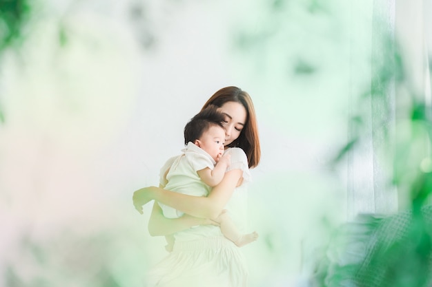 Mamma asiatica che tiene in braccio un bambino nella stanza luminosa