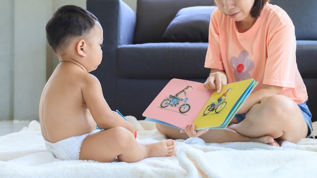 家でかわいい男の子と一緒に本を教えたり読んだりするアジア人のお母さん。家族と一体感の概念