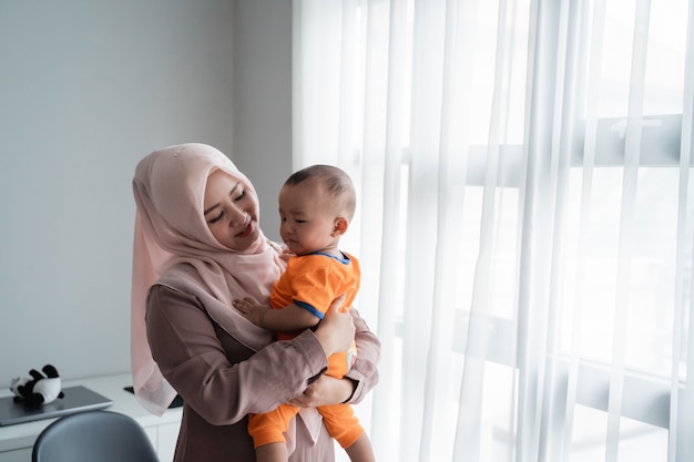 Asian moslem mother carrying her little boy when playing near window