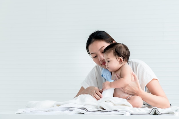 La madre asiatica attraente e giovane sta applicando il borotalco a sua figlia di 7 mesi dopo il bagno