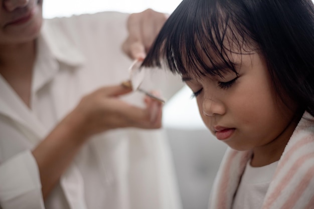 Asian Mother cutting hair to her daughter in living room at home while stay at home safe from Covid19 Coronavirus during lockdown Selfquarantine and social distancing concept