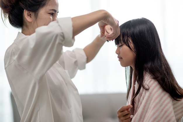 Asian Mother cutting hair to her daughter in living room at home while stay at home safe from Covid19 Coronavirus during lockdown Selfquarantine and social distancing concept