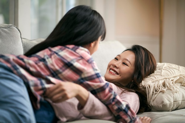 asian mother and daughter lying on couch and chatting at home