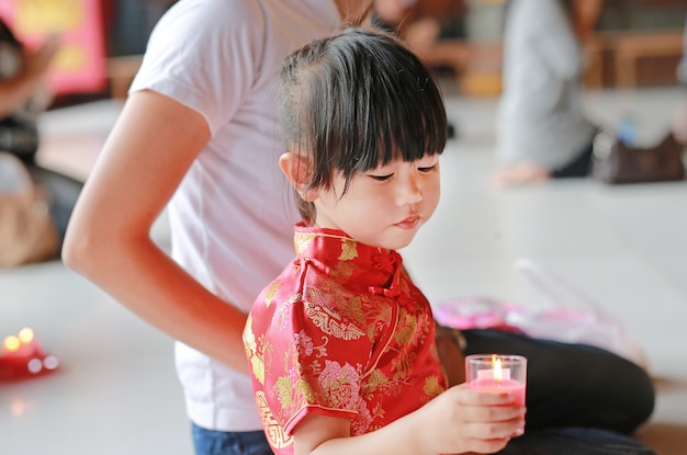 Asian mother and daughter in traditional dress light the worship candles at chinese temple