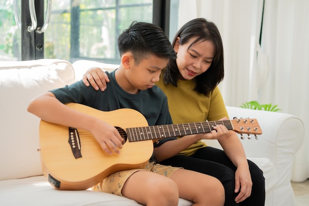 Asian mother embraces son Asian boy playing guitar and mother embrace on the sofa