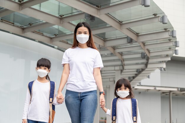 アジアの母親は、娘が保護のために医療用マスクを着用するのを手伝っていますCovid19の発生