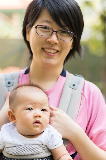 Asian  mother and her baby girl in a baby carrier, outdoors portrait