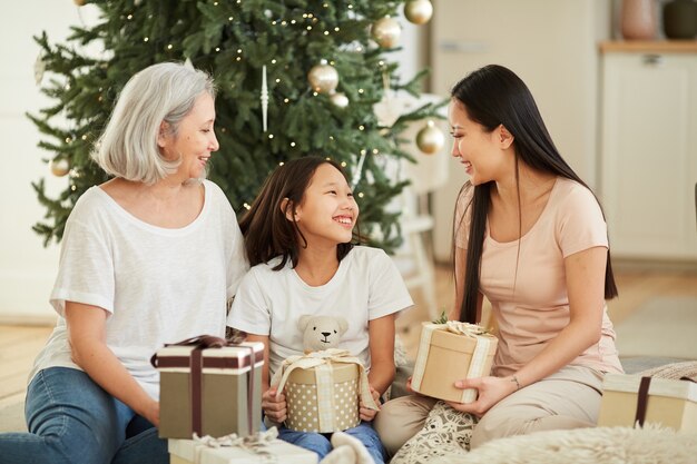 Asian mother and her daughter with granddaughter congratulating each other with Christmas and giving presents sitting on the floor