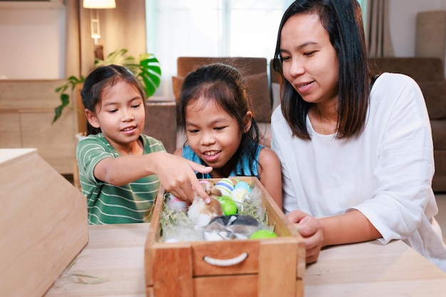 Asian mother and her daughters are playing with baby bunny and\
decorating easter eggs preparing for easter at home happy family\
happy easter happy holiday