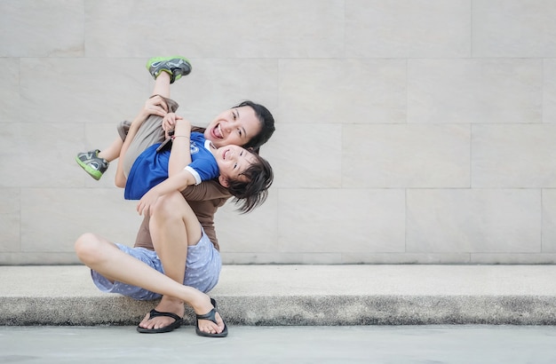  asian mother holding her son in fun motion on marble wall textured 