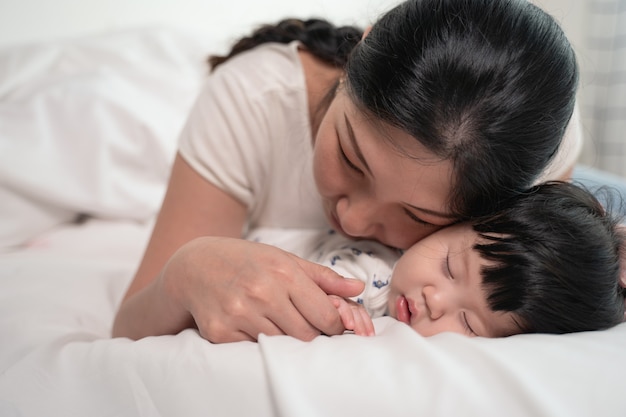 Asian mother kissing and touching a baby that sleeping on bed with gently and love