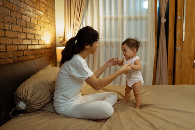 Asian mother playing with her baby on the bed