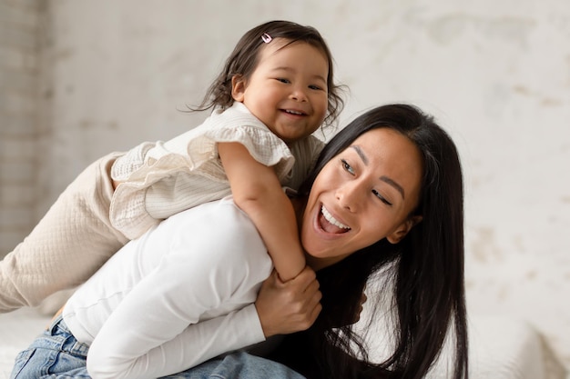 Asian mother riding little baby daughter on back in bedroom