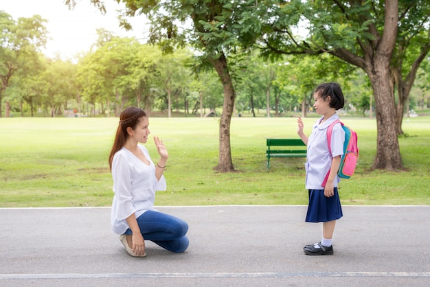 아시아 어머니는 공부하기 전에 학교에서 공원에서 딸 학생에게 작별 인사를합니다.