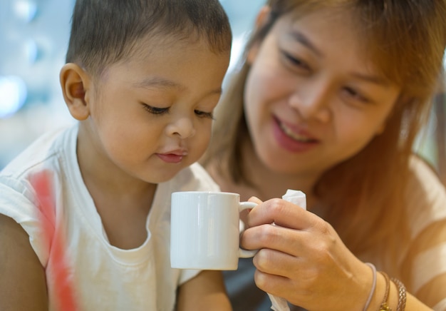 Photo asian mother and son. the mother was raised a white cup of water.