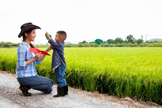 Madre e figlio asiatici che l'agricoltore giocano felicemente ad aeroplanini di carta con suo figlio nelle verdi risaie