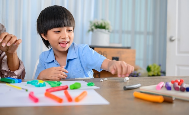 アジア人の母親は息子と一緒に家で働きます。ママと子供は生地をします。粘土粘土モデルを作成する子。女性のライフスタイルと家族の活動。