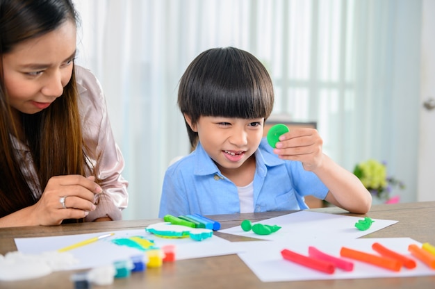 Asian mother work home together with son. Mom and kid play dough. Child creating plasticine clay model. Woman lifestyle and family activity.