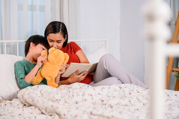 아시아 어머니는 아들과 함께 집에서 일합니다. 엄마와 아이는 침대에서 자기 전에 동화를 읽고 있습니다. 여성의 생활 방식과 가족 활동.
