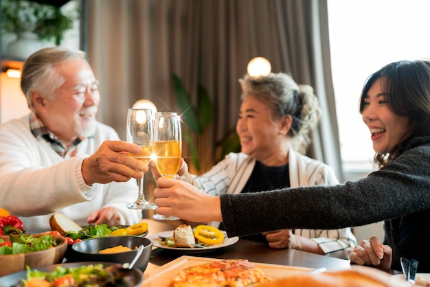 アジアの多世代の祖父母孫の幸せ楽しい夕食をホームホリデーのお祝いで一緒に、人々はクリスマスの感謝祭のディナーを持っている線香花火と幸せな友達をコンセプトします