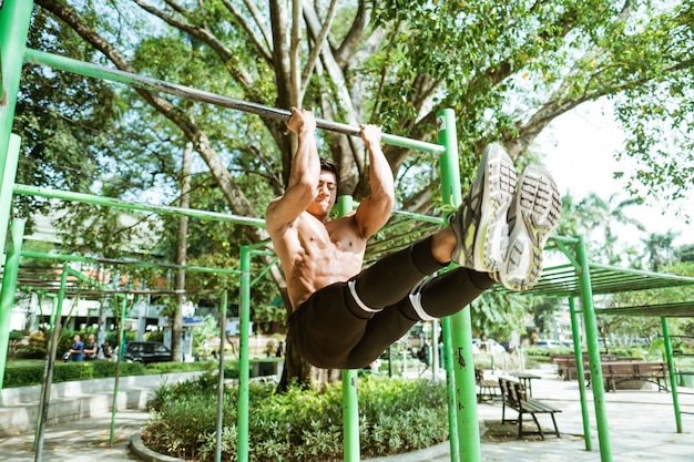 An asian muscular man without clothes doing L pull-up exercises using iron bar in the park