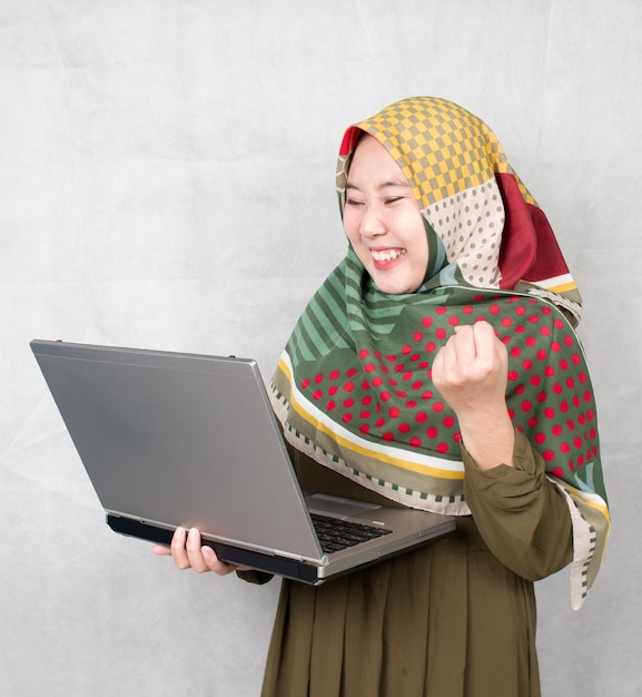 asian muslim adult woman being happy and surprised by something from laptop