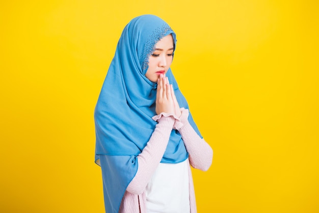 Asian muslim arab, portrait of happy beautiful young woman religious wearing veil hijab she henna decorated hands praying to allah god, isolated on yellow background, eid mubarak and soul fasting