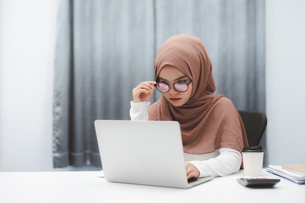 Asian muslim business woman wearing brown hijab working with laptop computer at home office.