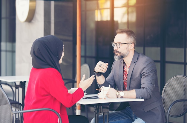 顧客またはボーイフレンドと話しているコーヒーショップでアジアのイスラム教徒の実業家