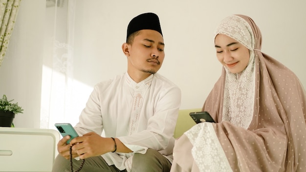 Asian muslim couple playing cell phone on sofa