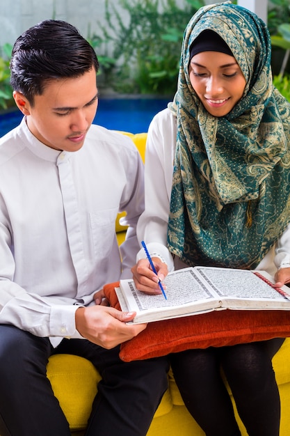 Asian Muslim couple reading together Koran or Quran 