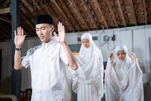 Asian muslim family praying jamaah together at home. sholat or salah wearing white and hijab