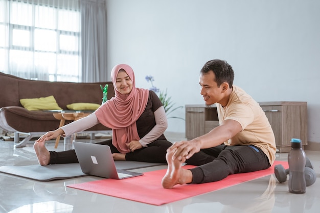 Asian muslim fitness couple stretching and looking at online video tutorial via laptop