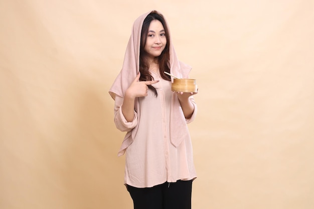 Asian Muslim girl smiles with her hand gesturing to the bowl and holding the wooden bowl in front of