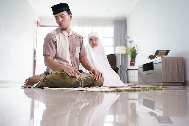 Asian muslim husband and wife praying jamaah together at\
home